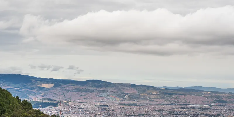 Bogotá seen from above, dense city blocks running back to the green hills behind it